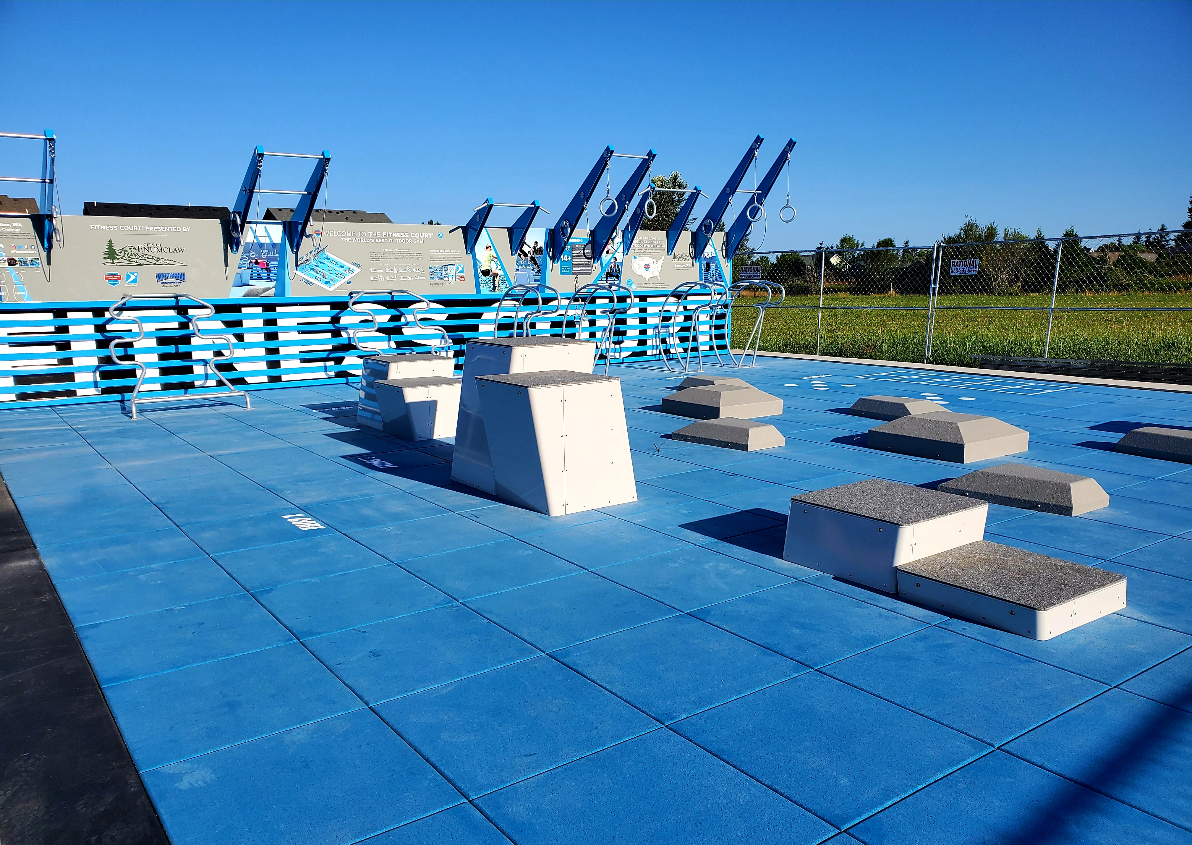 Outdoor fitness court featuring metal bars and rings, as well as concrete platforms of various heights